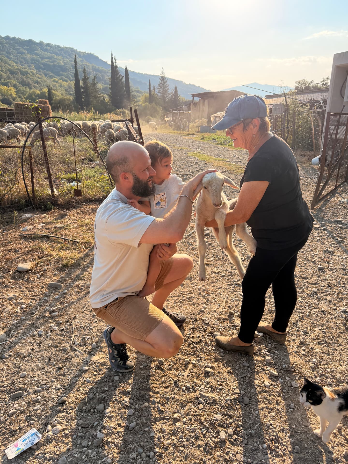 אבא והפעוט מלטפים גדי קטן שהרועה מחזיקה בחווה
